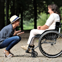 Un joven arrodillado y alegrando a una persona en silla de ruedas